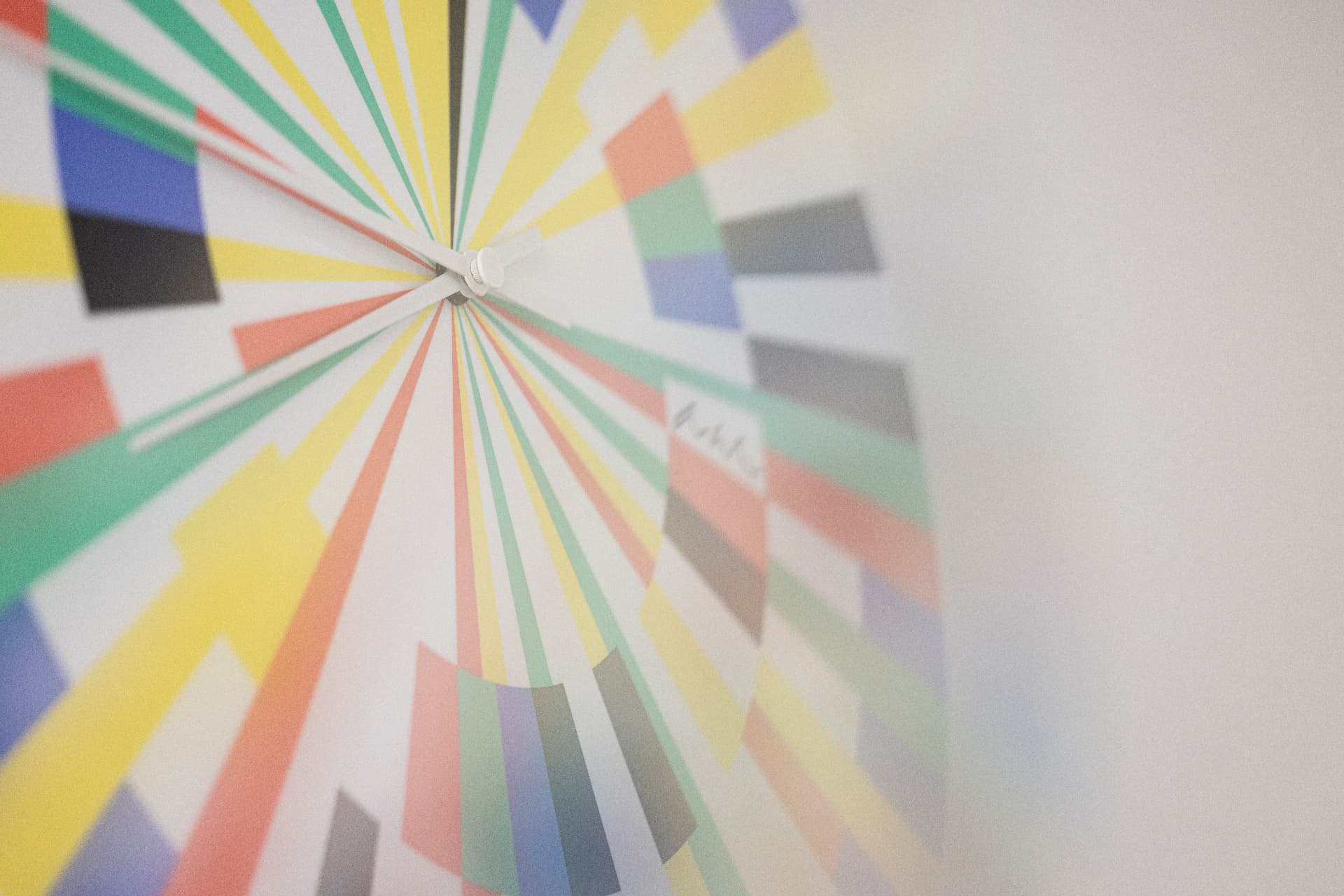 Colourful radial clock in yellow, red, green and blue on a white wall