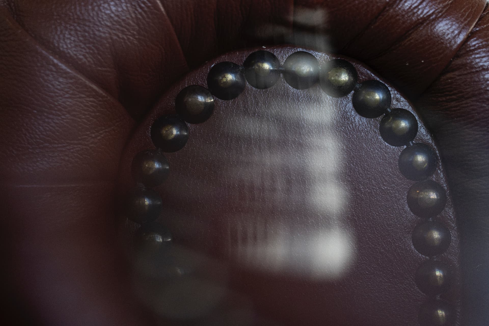 Close-up of a brown leather armchair with decorative studs behind glass