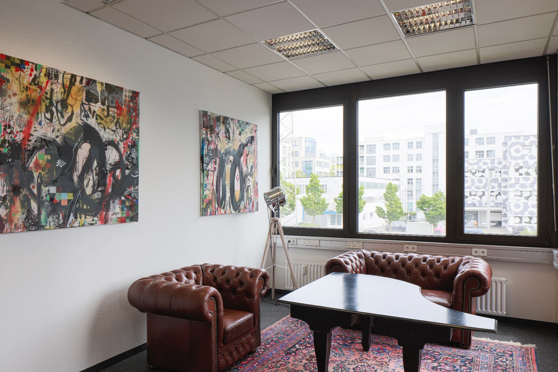 Gallery with brown Chesterfield armchairs, large-format paintings and window front